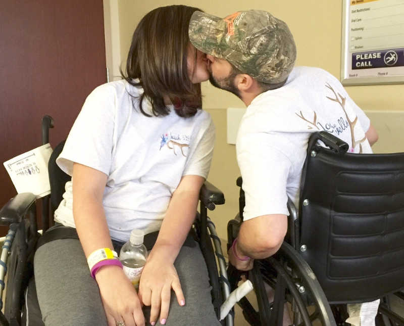 Woman who suffered amnesia in car accident sits in wheel chair kissing her husband who is also in wheel chair