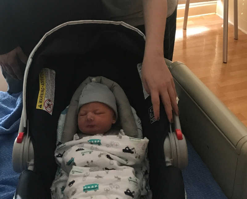 Newborn lays asleep in car seat while mother who escaped death places hand on car seat
