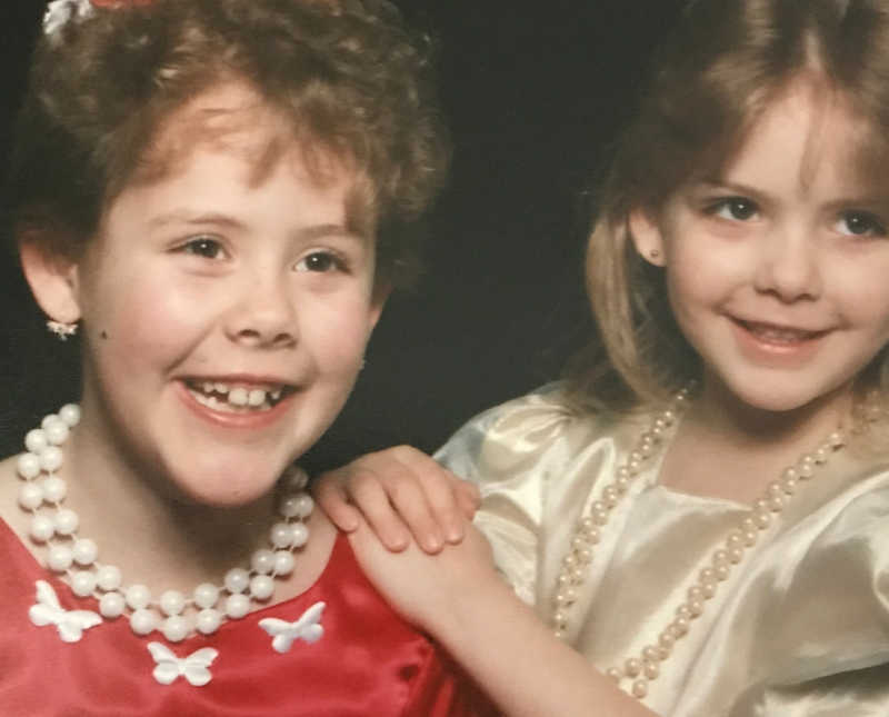 Two little girls in formal dresses and pearl necklaces smile beside each other