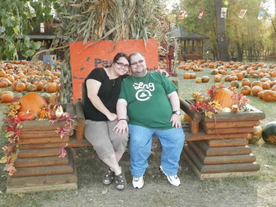 Husband and wife who met on dating website sit outside on bench in pumpkin patch