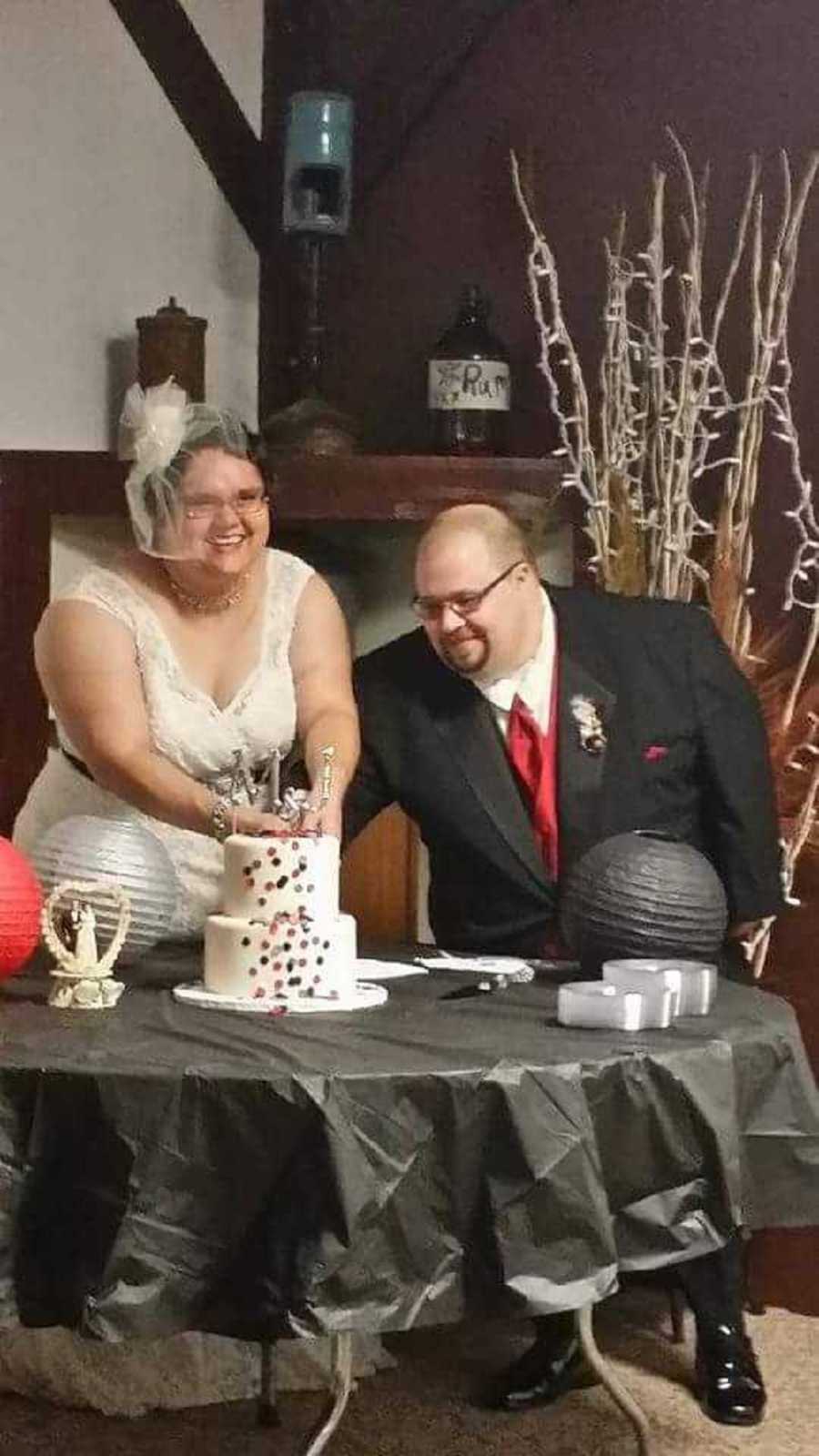 Bride and groom smile as bride cuts their wedding cake