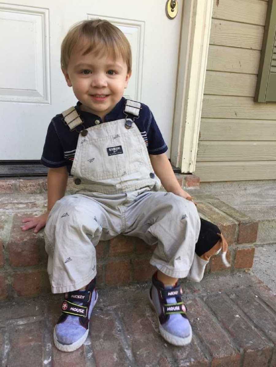 Toddler boy sits smiling on step outside of home 