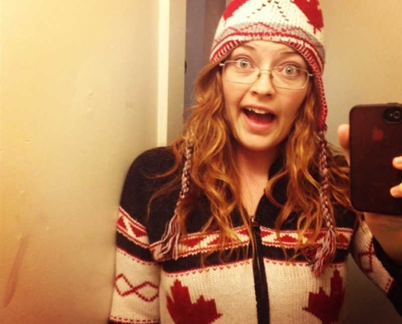 Young woman smiles in mirror selfie while wearing winter sweater and hat