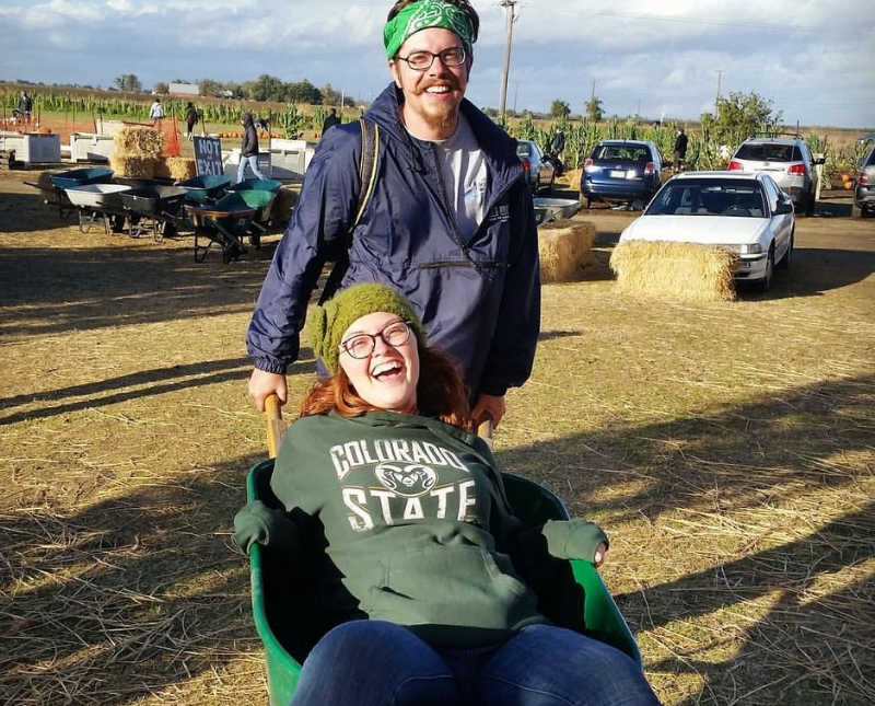 Young woman with Thoracic Outlet Syndrome sits in hay bale being pushed by boyfriend