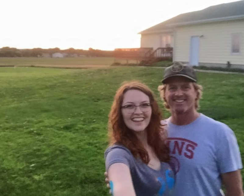 Young woman stands smiling in selfie beside father in their yard