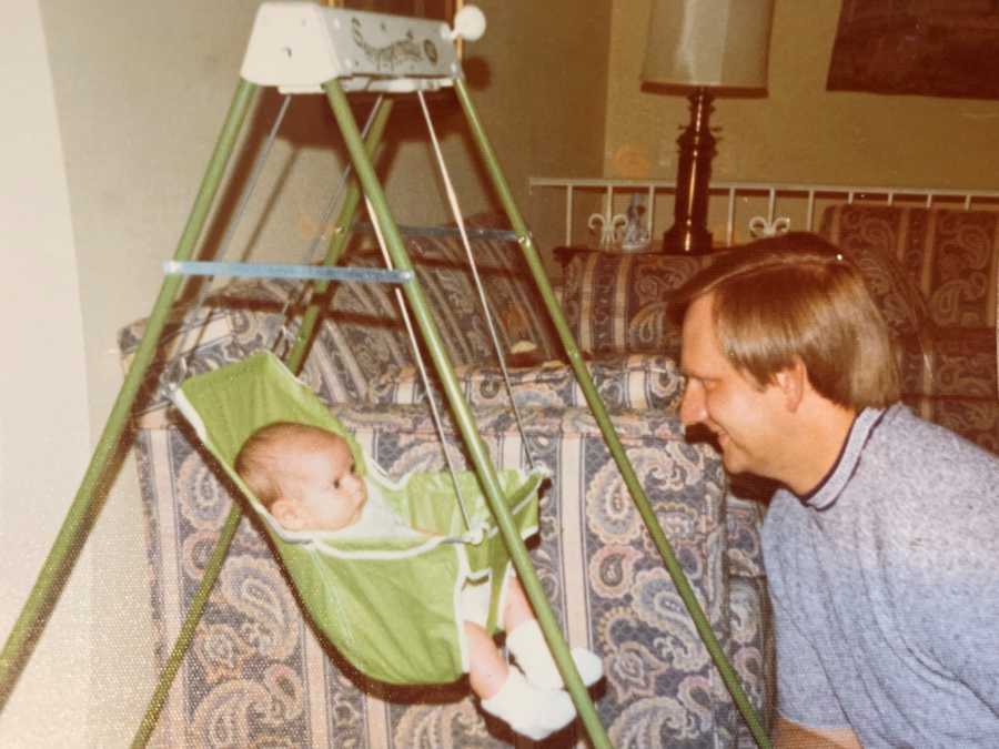 Baby sits in baby swing looking at adoptive father in home