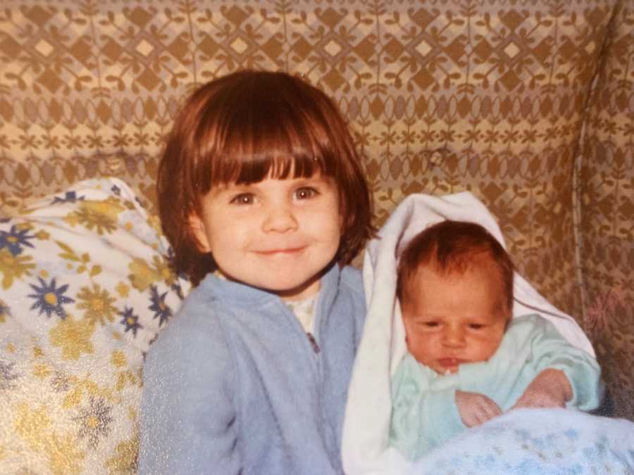 Adopted little girl sits in chair smiling with baby sister in her lap