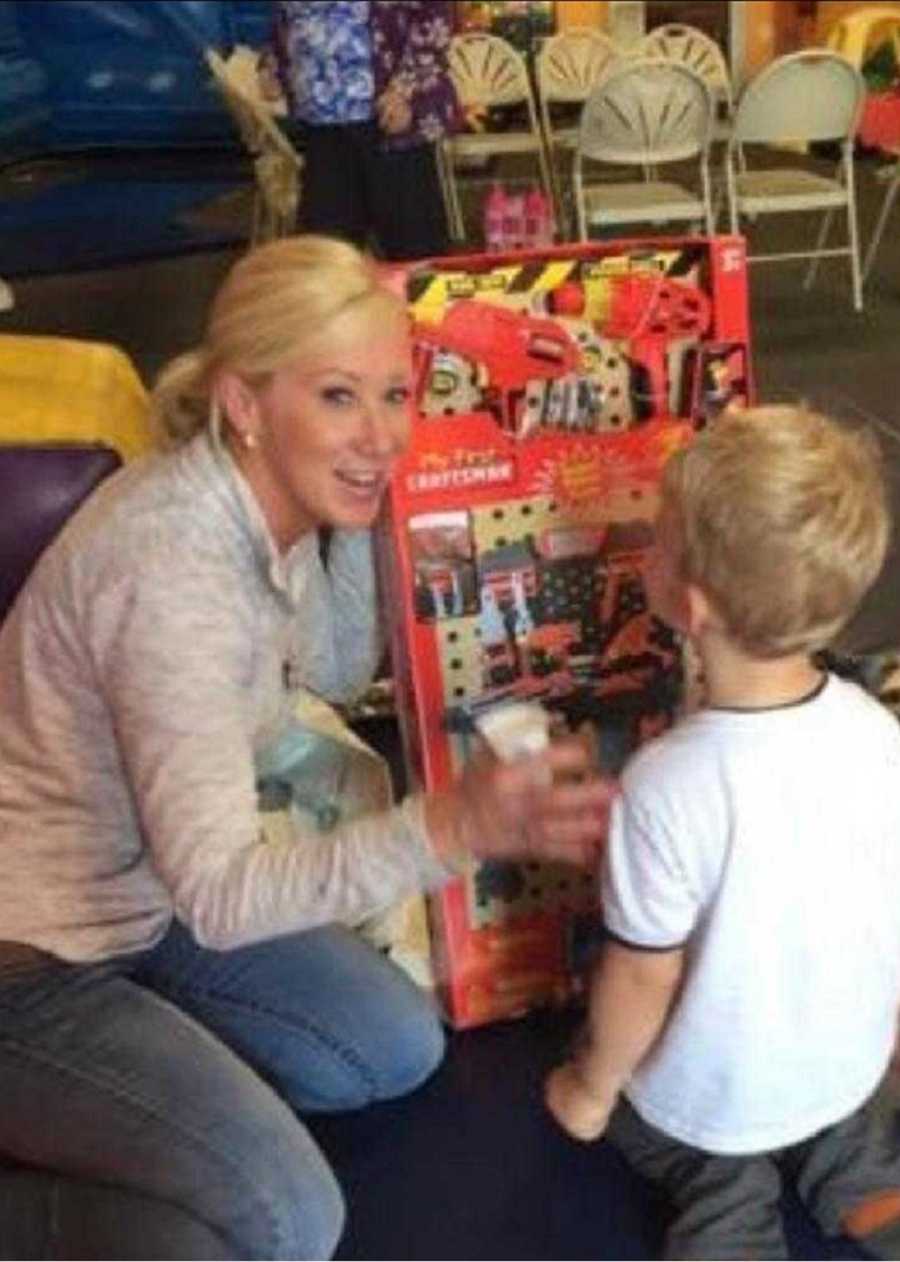 Woman smiles as she sits on floor of classroom with little boy