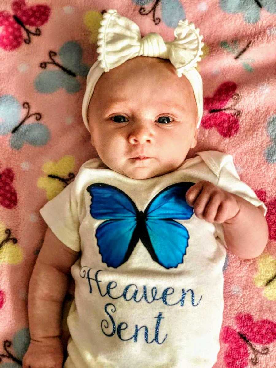 Newborn baby girl lays on back on blanket wearing a onesie with blue butterfly that represents her deceased aunt