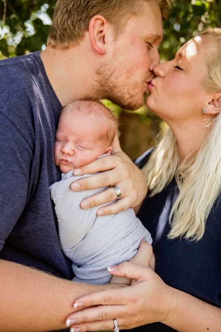 Husband holds newborn while he kisses wife with Hodgkin's lymphoma