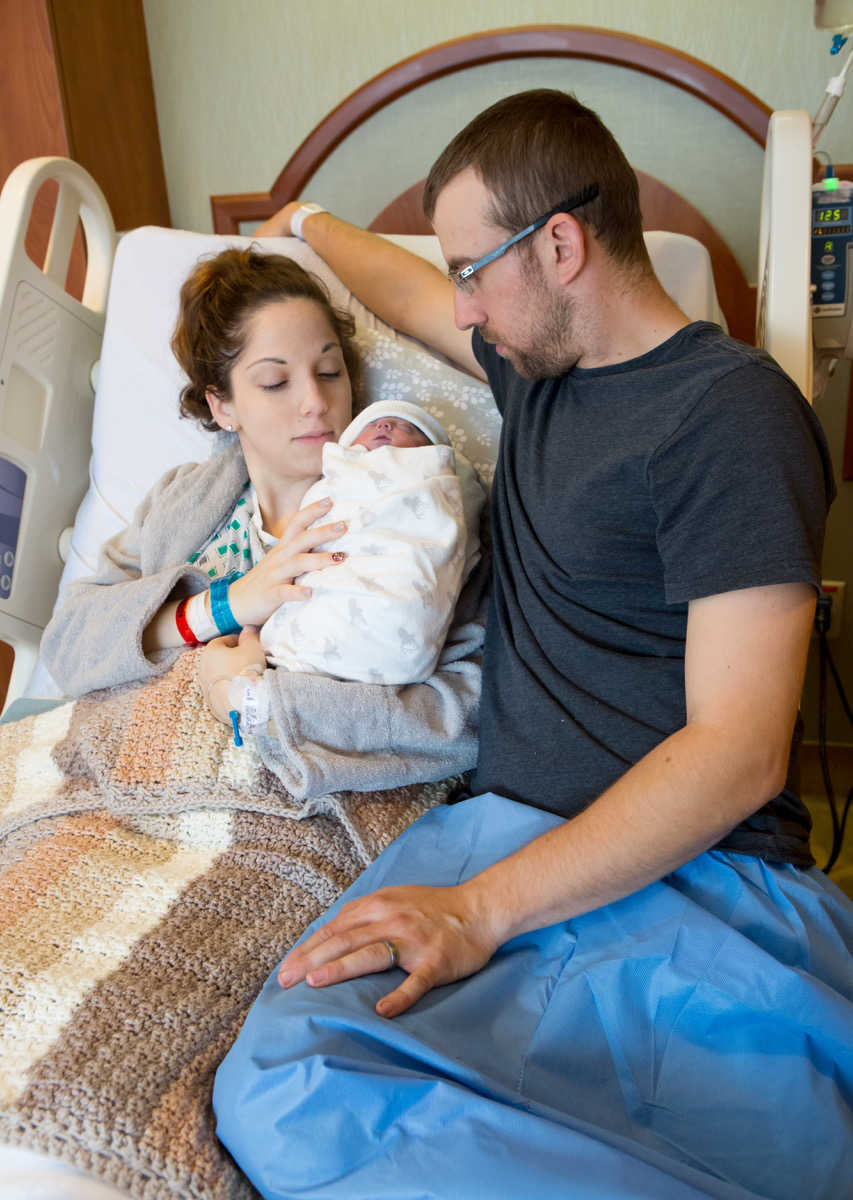 Woman lays in hospital bed beside her newborn and husband 