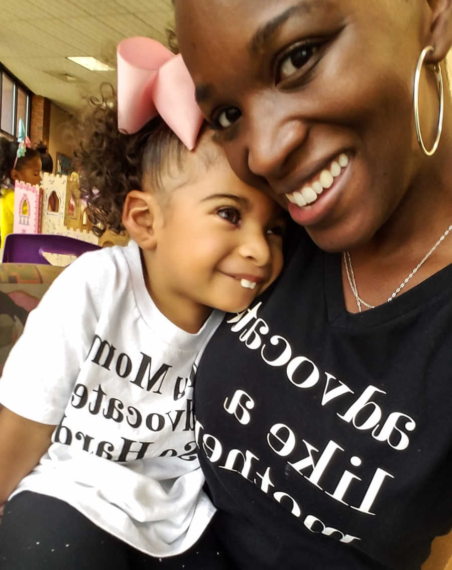 Little girl with prosthetic eyes sits smiling on her mothers lap while mother takes selfie