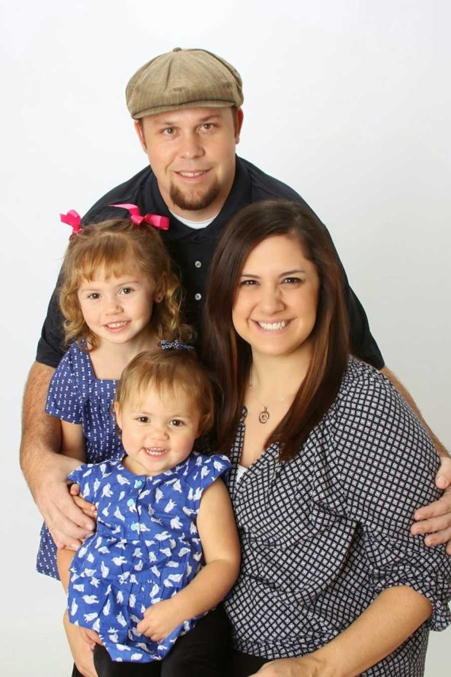 Husband and wife smile with their two daughters for family portrait