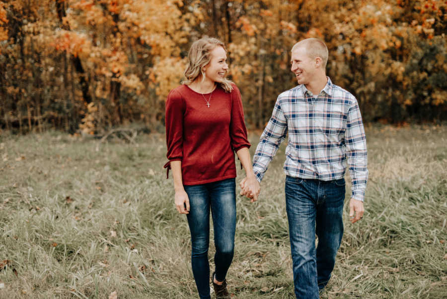 Couple who struggled to get pregnant smile at each other as they walk in yard holding hands