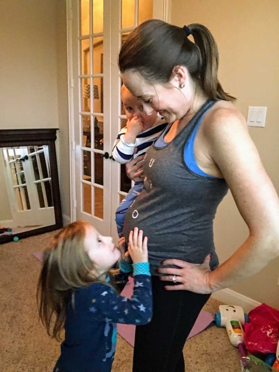 Pregnant woman stands holding son while daughter stands touching her mother's stomach