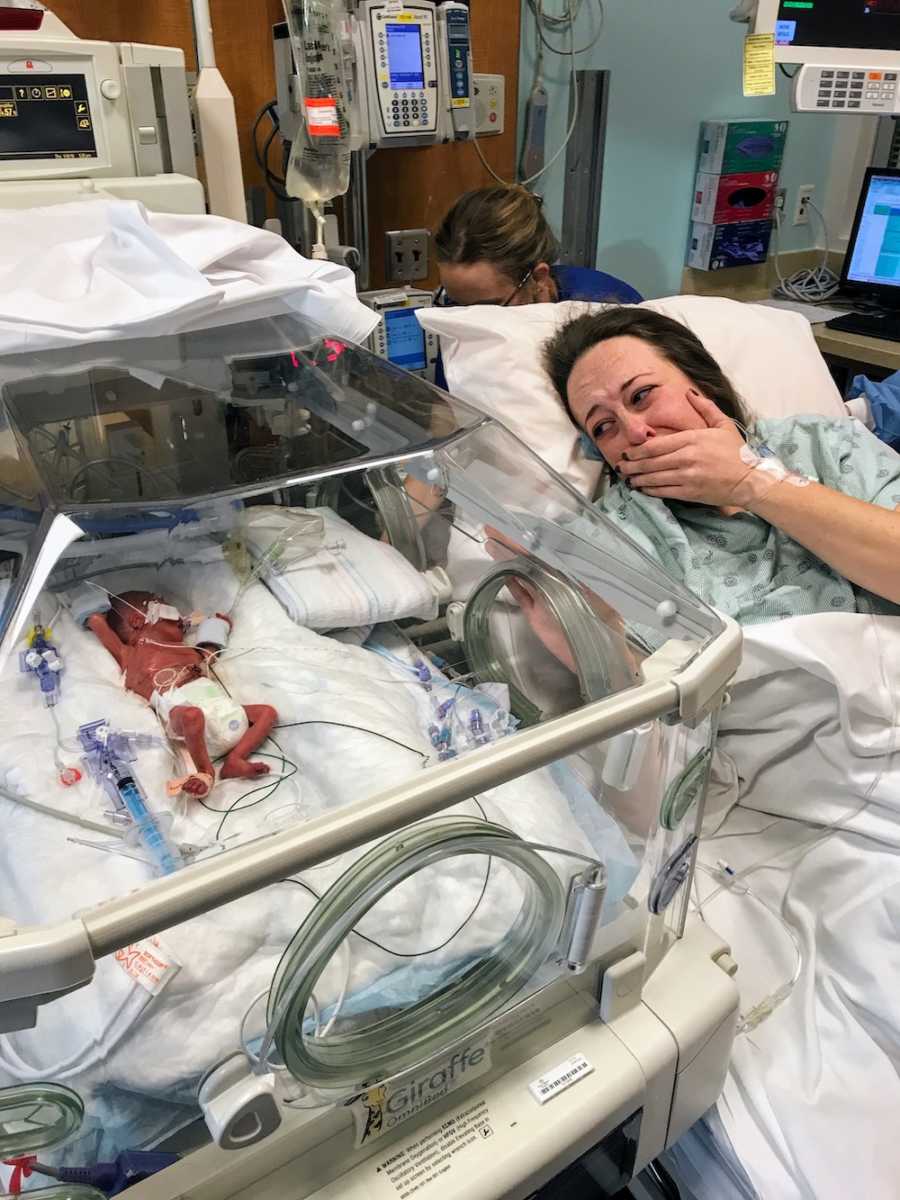 Mother cries as she lays in hospital bed looking over at newborn who was immediately intubated