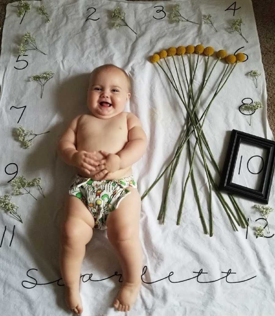 Baby girl smiling as she lays on her back on blanket that indicates that she is 10 months