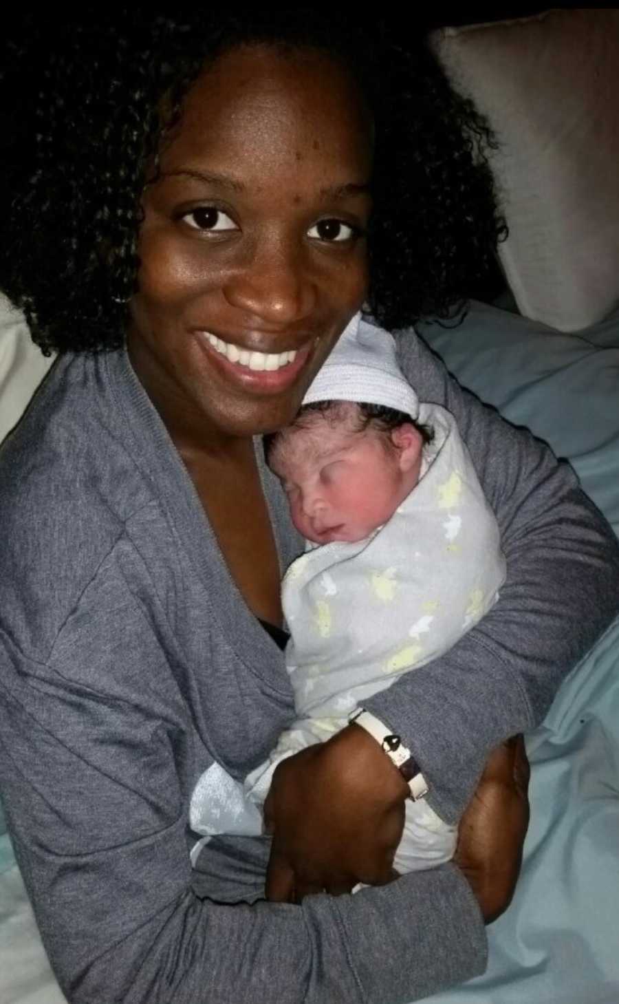 Mother smiles as she holds newborn baby asleep in her arms