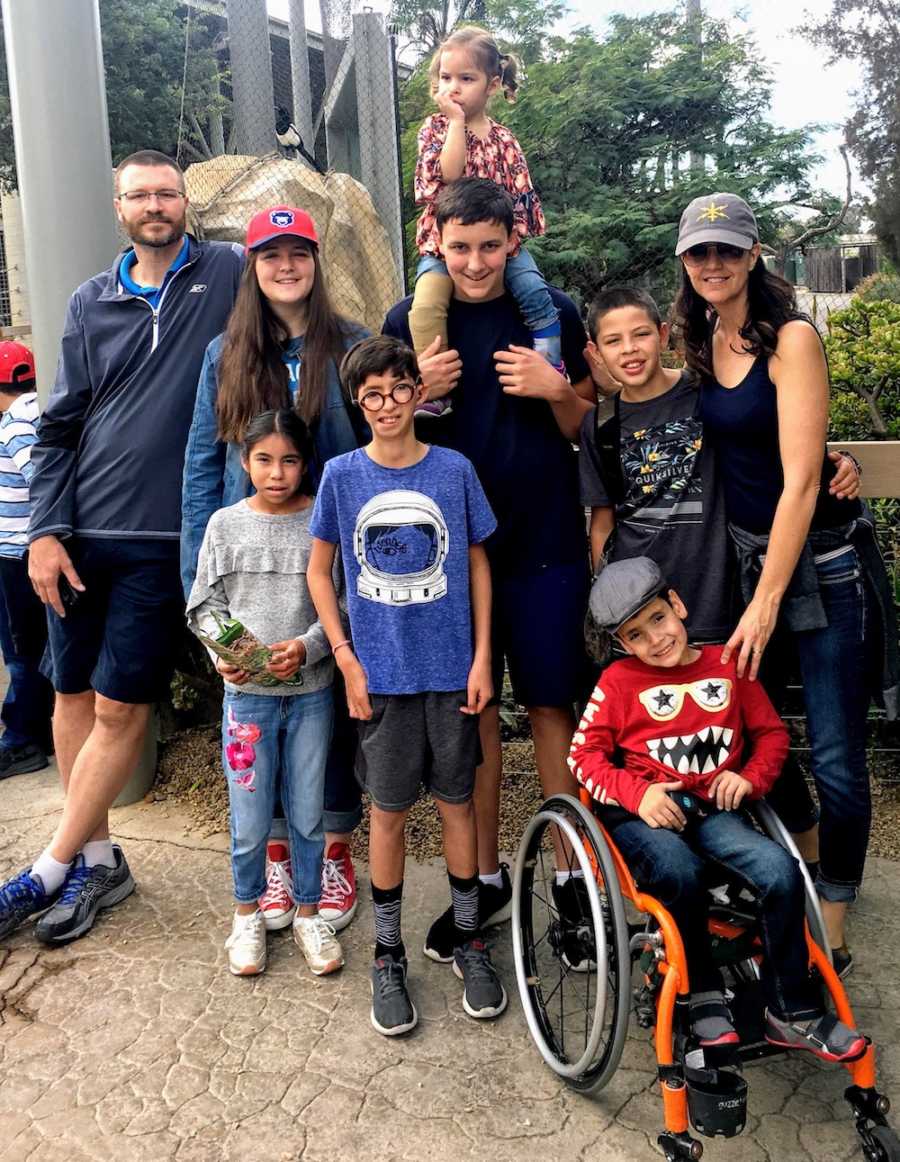 Husband and wife stand outside with their two biological kids and four foster kids who are siblings