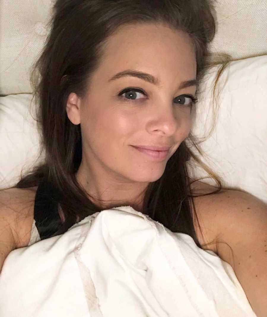 Woman who has anxiety and depression smiles as she takes selfie in bed