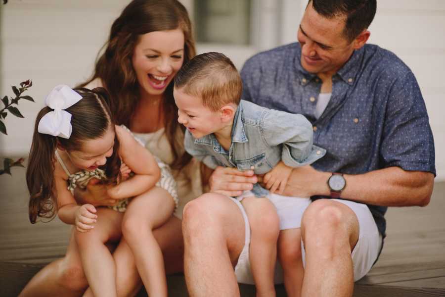 Woman who has anxiety and depression smiles as she sits beside her husband with their two kids on their laps