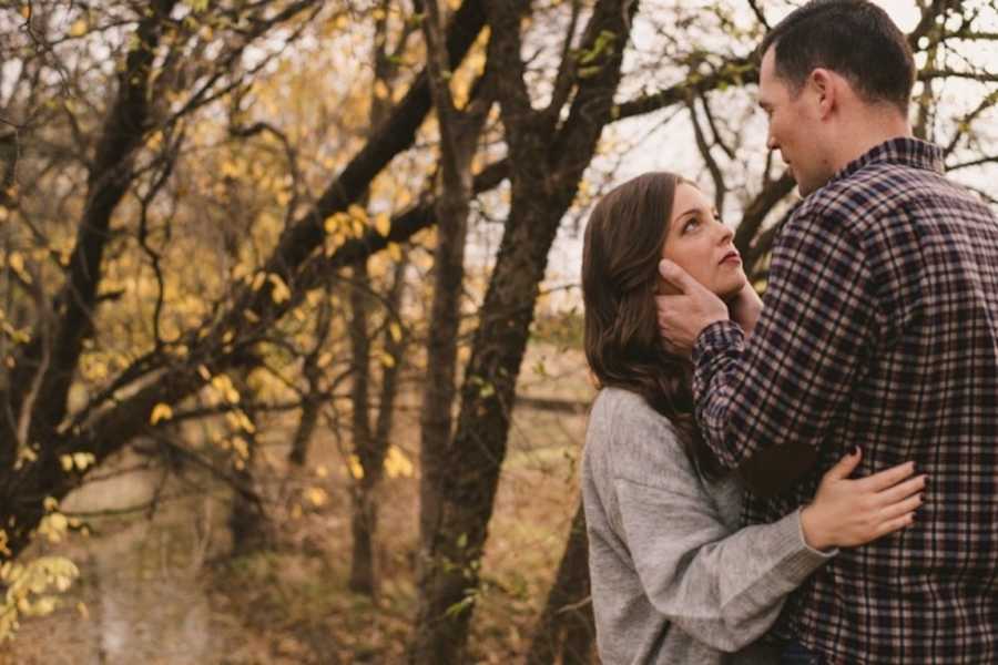 Wife with body dysmorphia stands in wooded area looking up at husband who holds her face