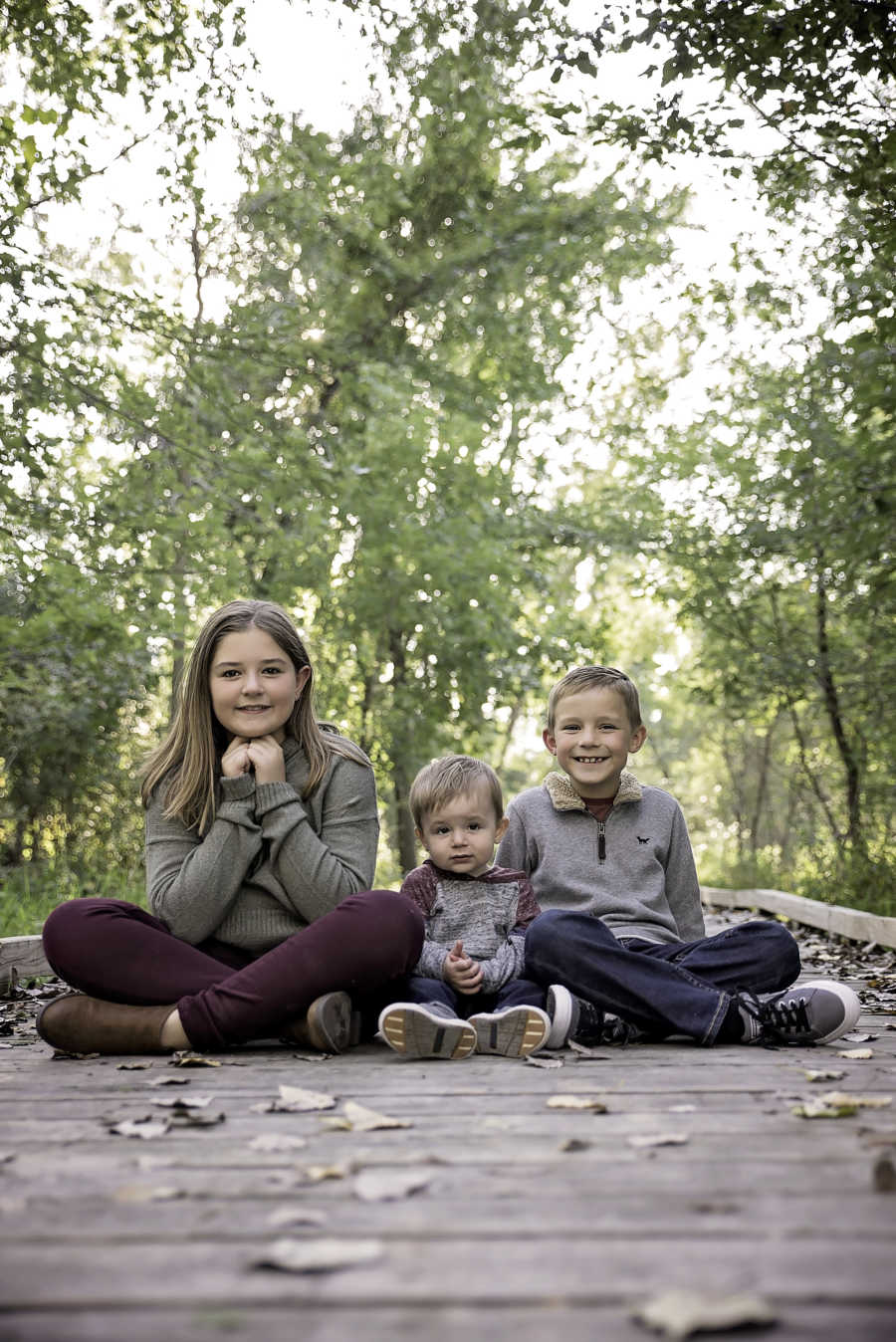 Three siblings sit on wooden bridge whose father is dead