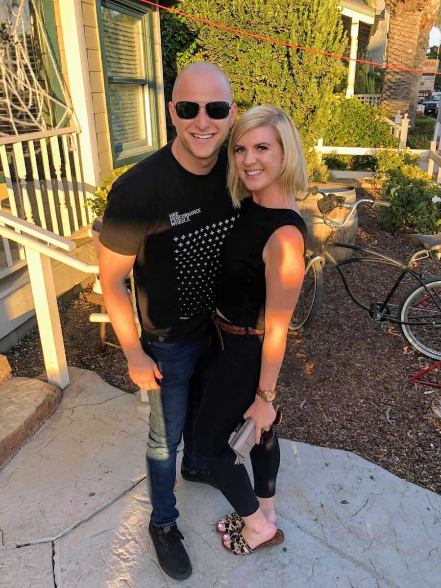 Woman who found a lump on her breast stands outside home smiling beside boyfriend