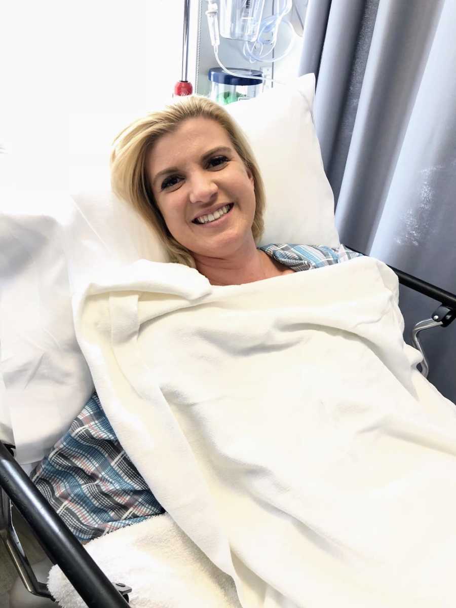 Woman smiles as she lays in hospital bed awaiting chemotherapy