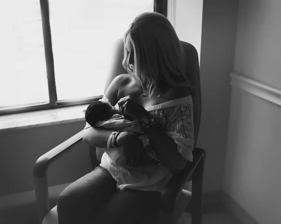 Woman sits in hospital room breast feeding adopted newborn