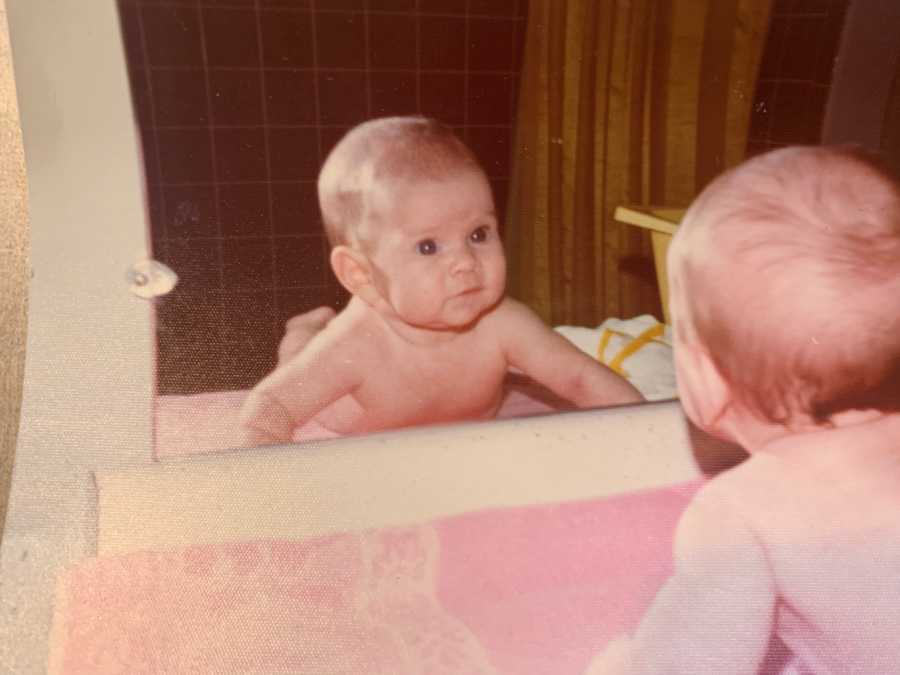 Baby lays on stomach looking at herself in mirror