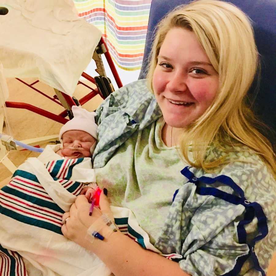 Woman smiles as she sits in NICU holding baby with Hypoplastic Left Heart Syndrome