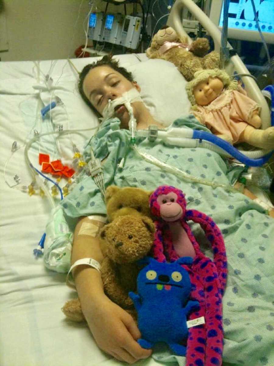 Intubated young woman lays in hospital bed in coma with stuffed animals at her side