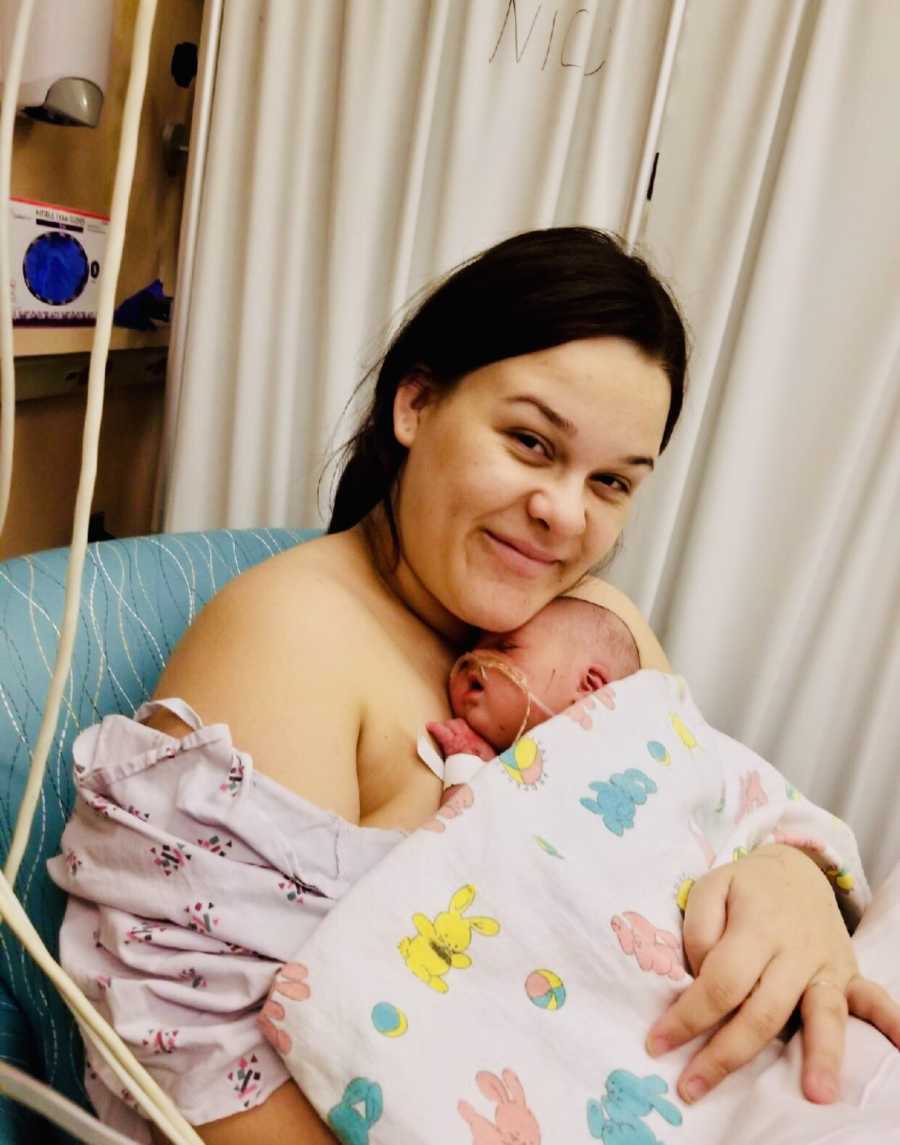 Mother sits in NICU smiling while her newborn with down syndrome lays asleep on her bare chest