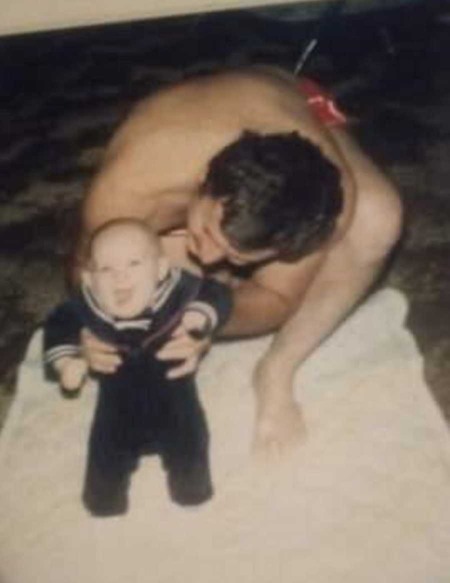 Man kneels on beach holding up his baby who he will later in life sexually abuse