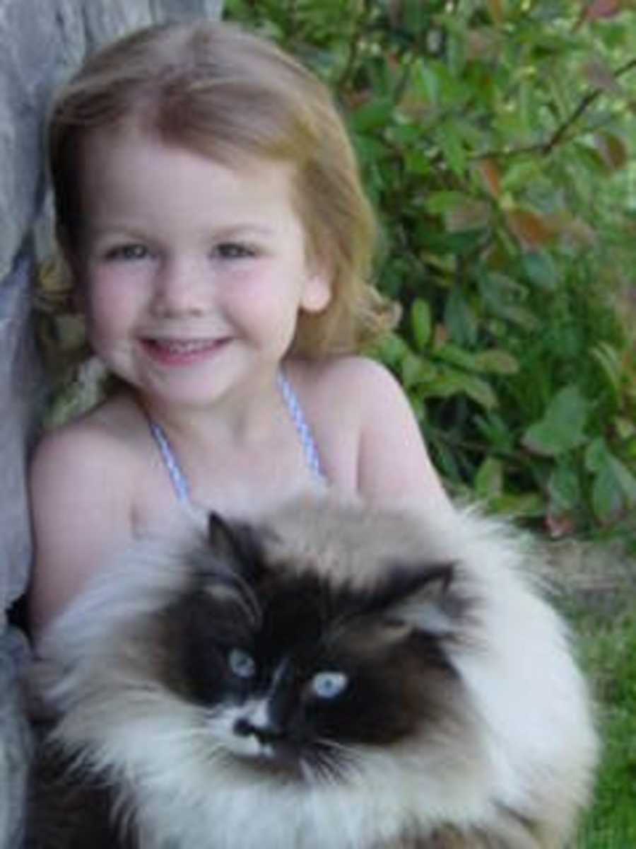 Little girl smiles as she sits outside with cat on her lap