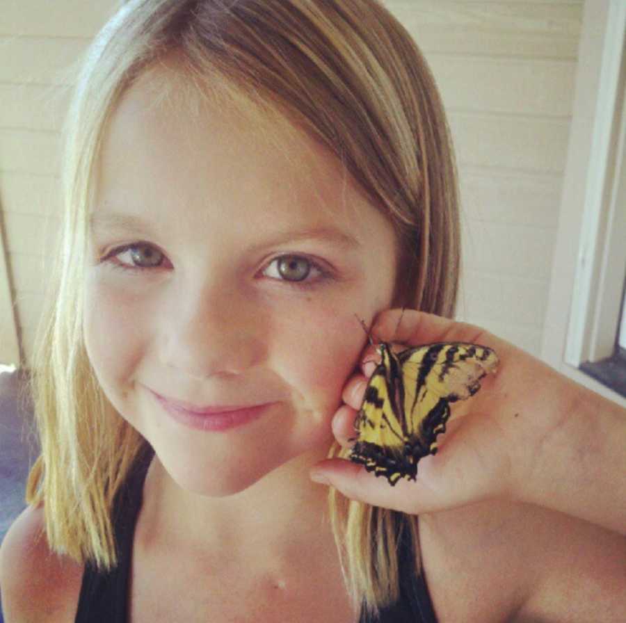 Little girl smiles as she holds yellow and black butterfly up to her face