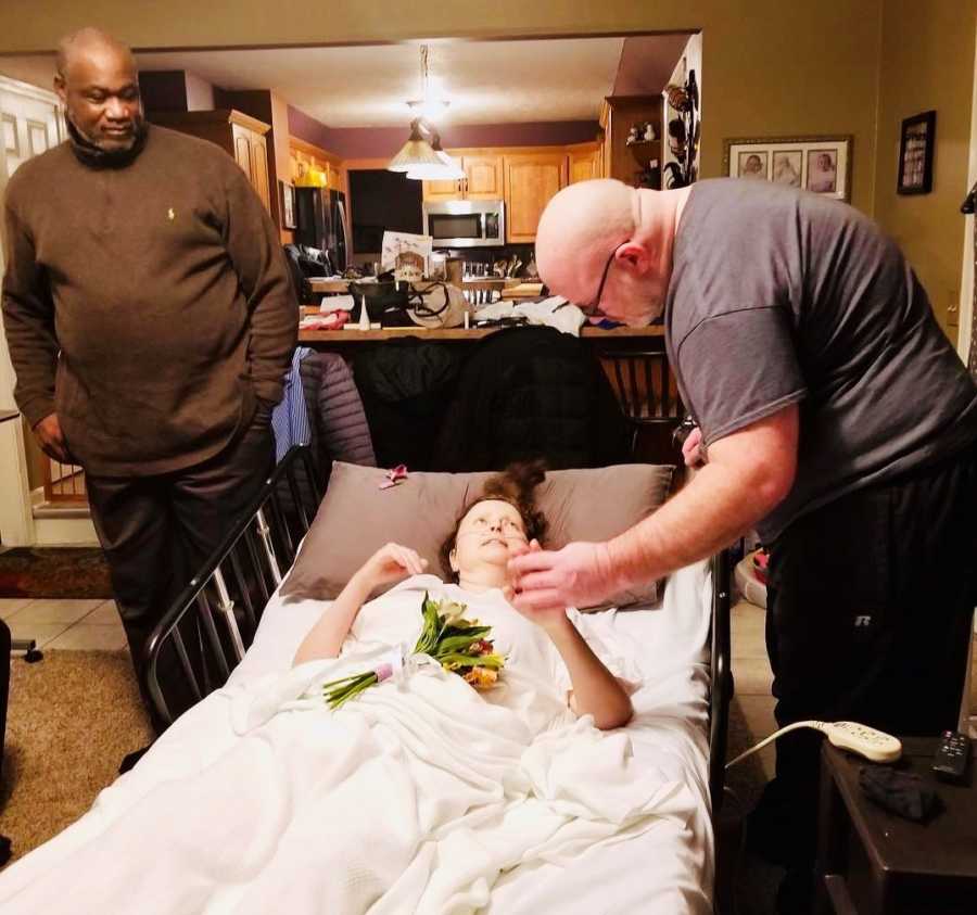 Woman with terminal cancer lays in hospital bed in home as she holds hands with her husband