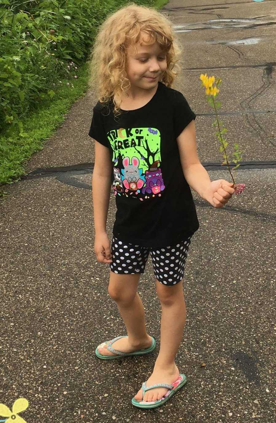 Little girl stands outside holding yellow flower