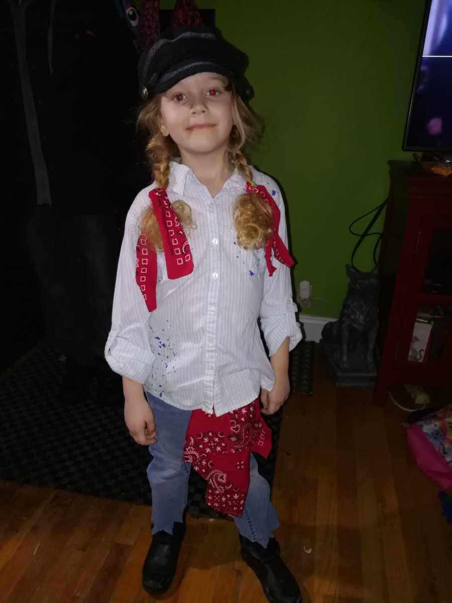Little girl stands in home wearing jeans with red bandana in her pants and in her braids