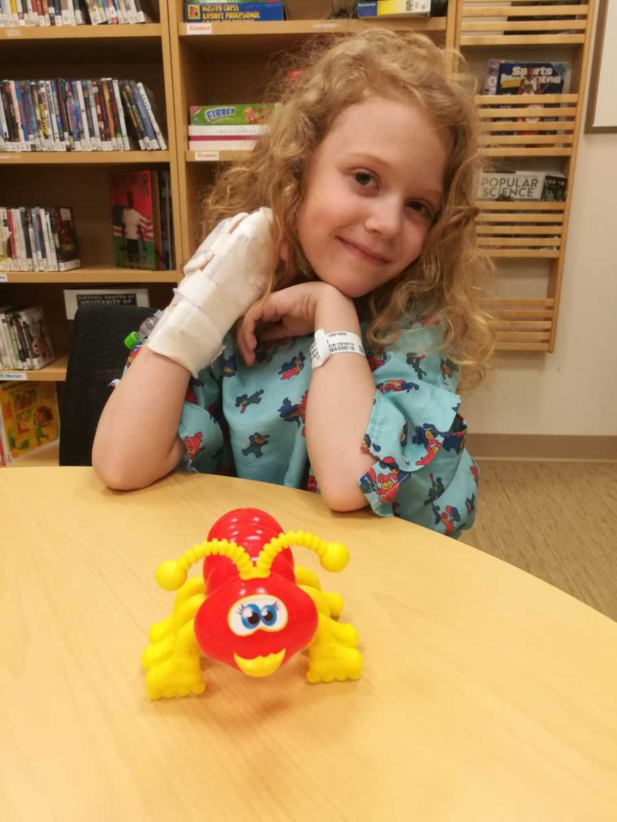 Little girl with brain cancer sits in hospital room with books and toys