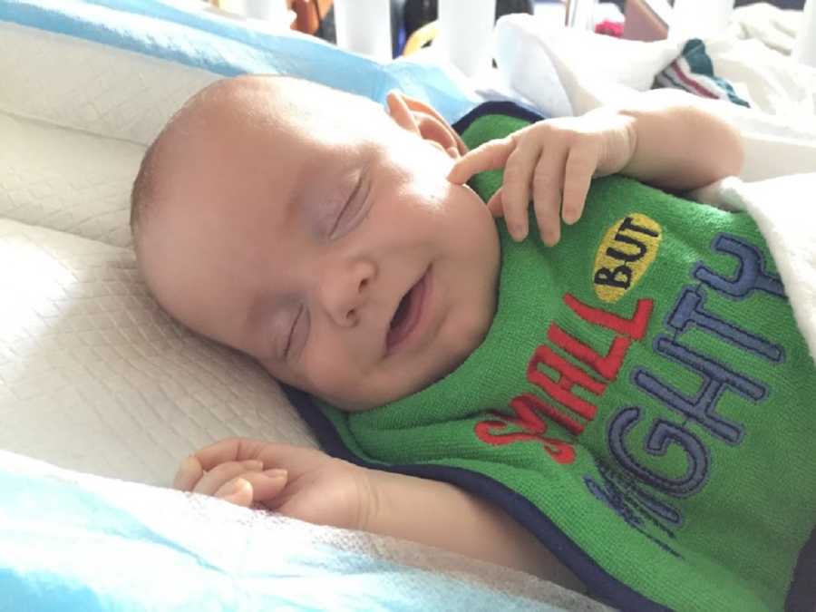 Baby smiles as he lays asleep with bib on