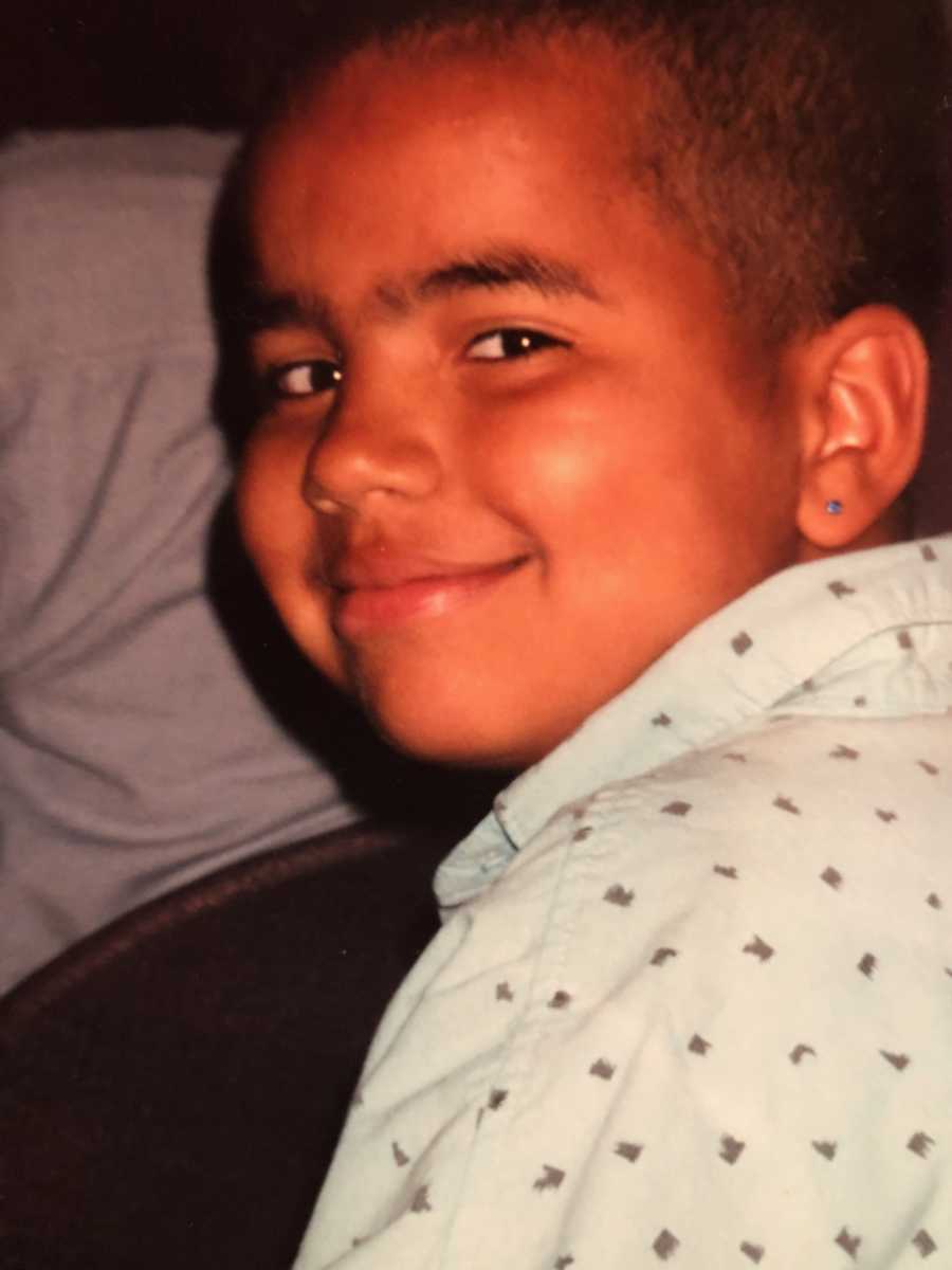 Little boy with ear pierced smiles over his shoulder