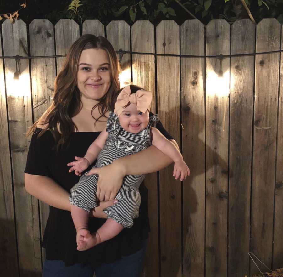 Mother smiles as she holds daughter with down syndrome outside in front of wooden fence
