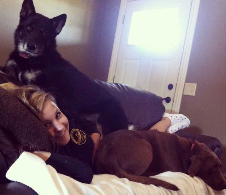 Woman smiles as she lays on couch with her two big dogs lying on either side of her