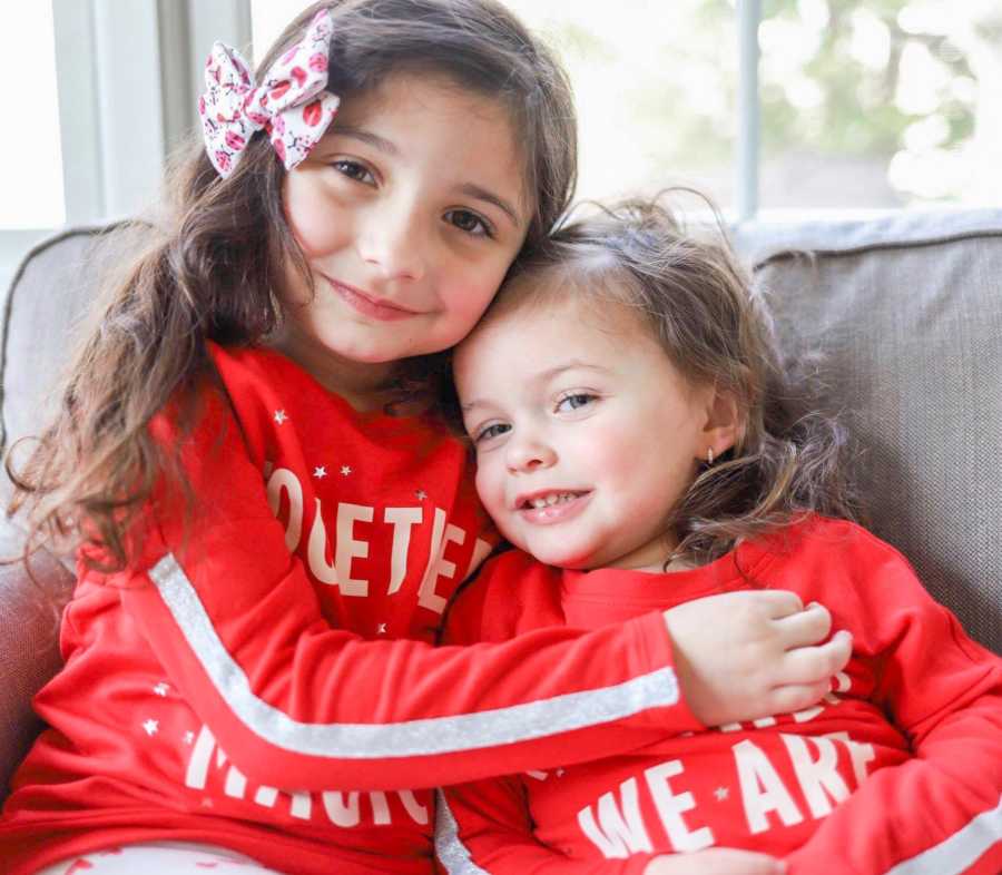 Little girl smiles as she sits in chair in home beside her younger sister