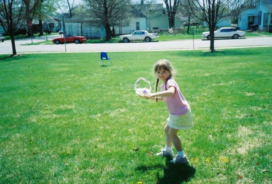 Little girl smiles as she stands in yard posing like she is going to throw what is in her hand