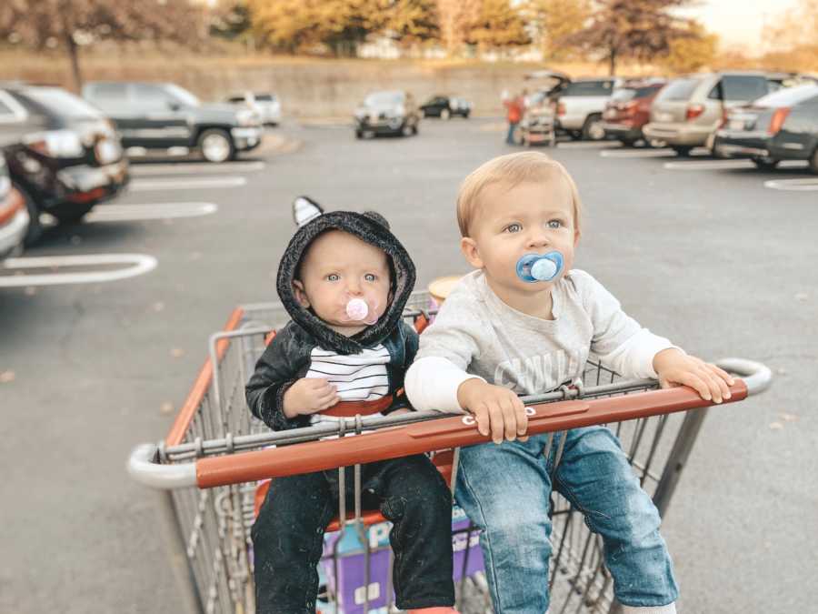 Baby brother and sister sit in shopping cart in parking lot