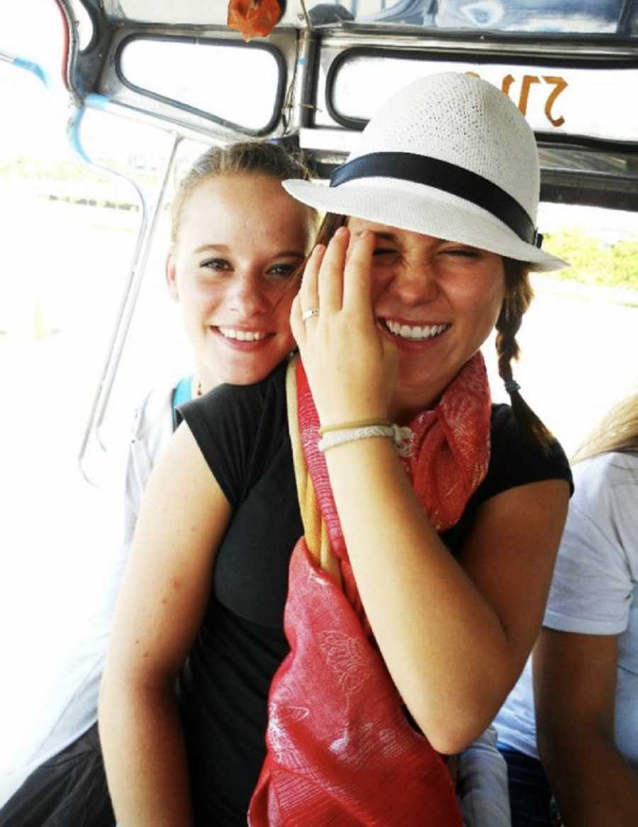 Young woman smiles as she sits on her friends lap