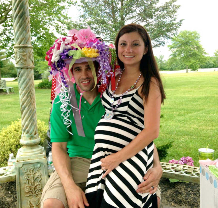 Pregnant woman stands outside as her husband with confetti hand on sits beside her